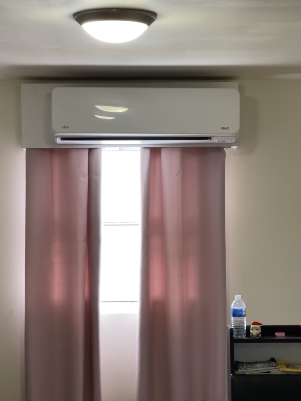 Fujitsu wall-mounted mini-split installed above a curtained window in a residential bedroom, clean white finish and tidy line set
