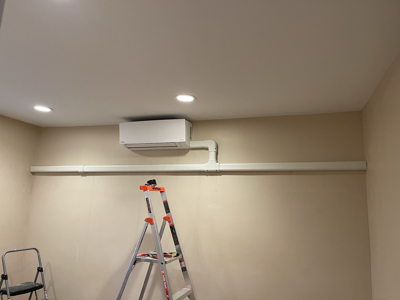 Daikin ductless mini-split air handler installed in a finished basement living area above a step ladder