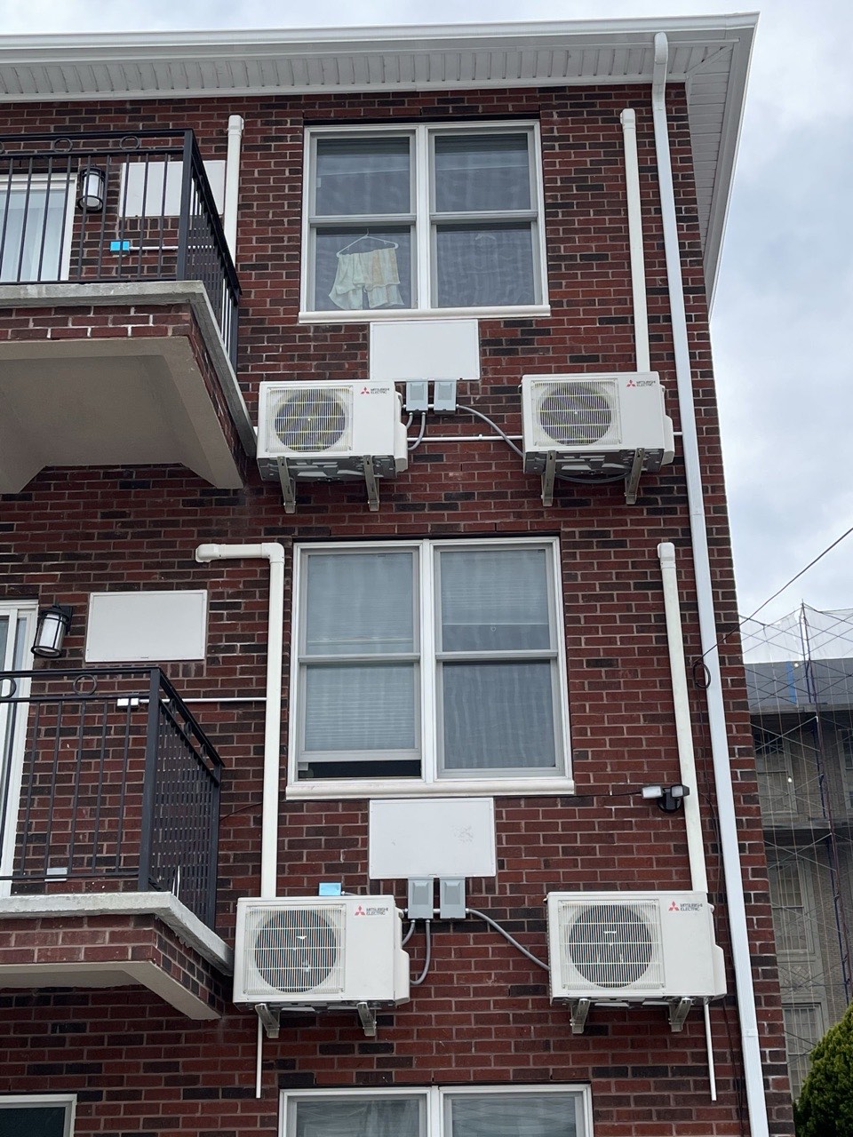 Four Mitsubishi Electric outdoor condensers wall-mounted on a multi-story Brooklyn brick apartment building