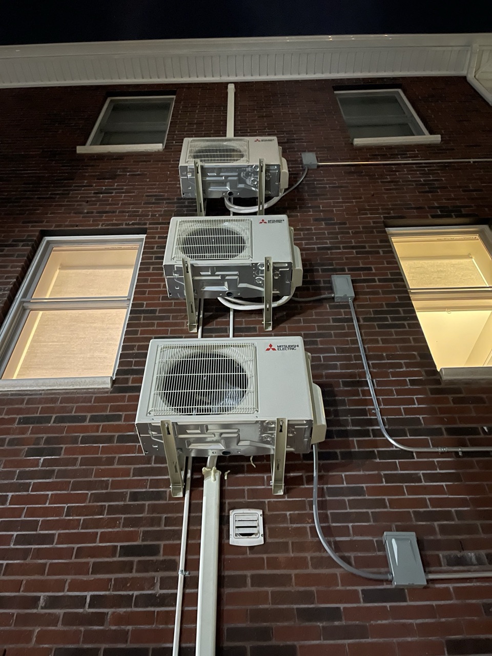 Three stacked Mitsubishi Electric outdoor condensers wall-mounted vertically on a Brooklyn brick building with shared line-set runs