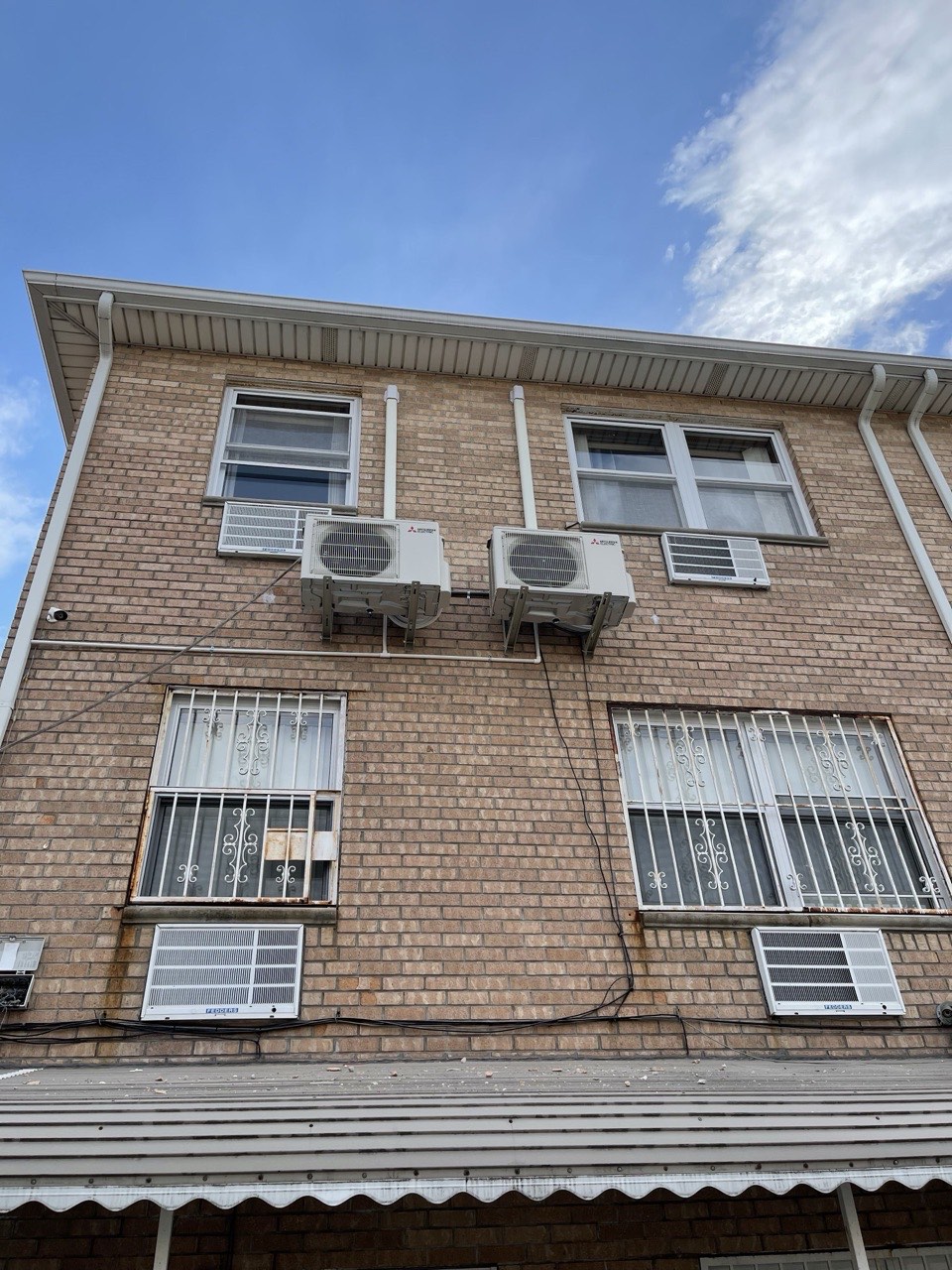Three Fujitsu outdoor condenser units wall-mounted on a Brooklyn brick rowhouse with window-mount AC units