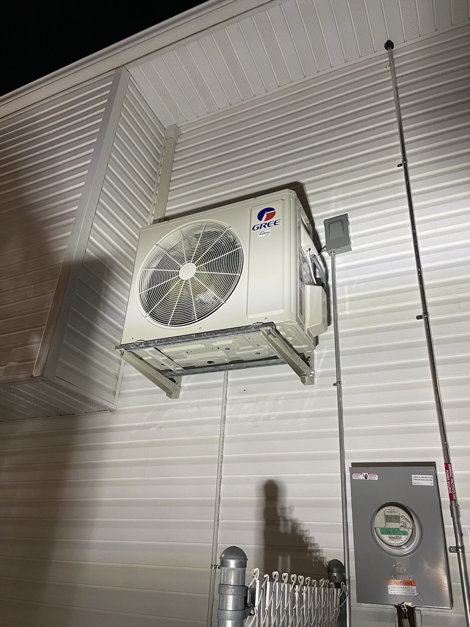 Gree outdoor condenser unit wall-mounted high on the white siding of a Brooklyn home with electric meter alongside