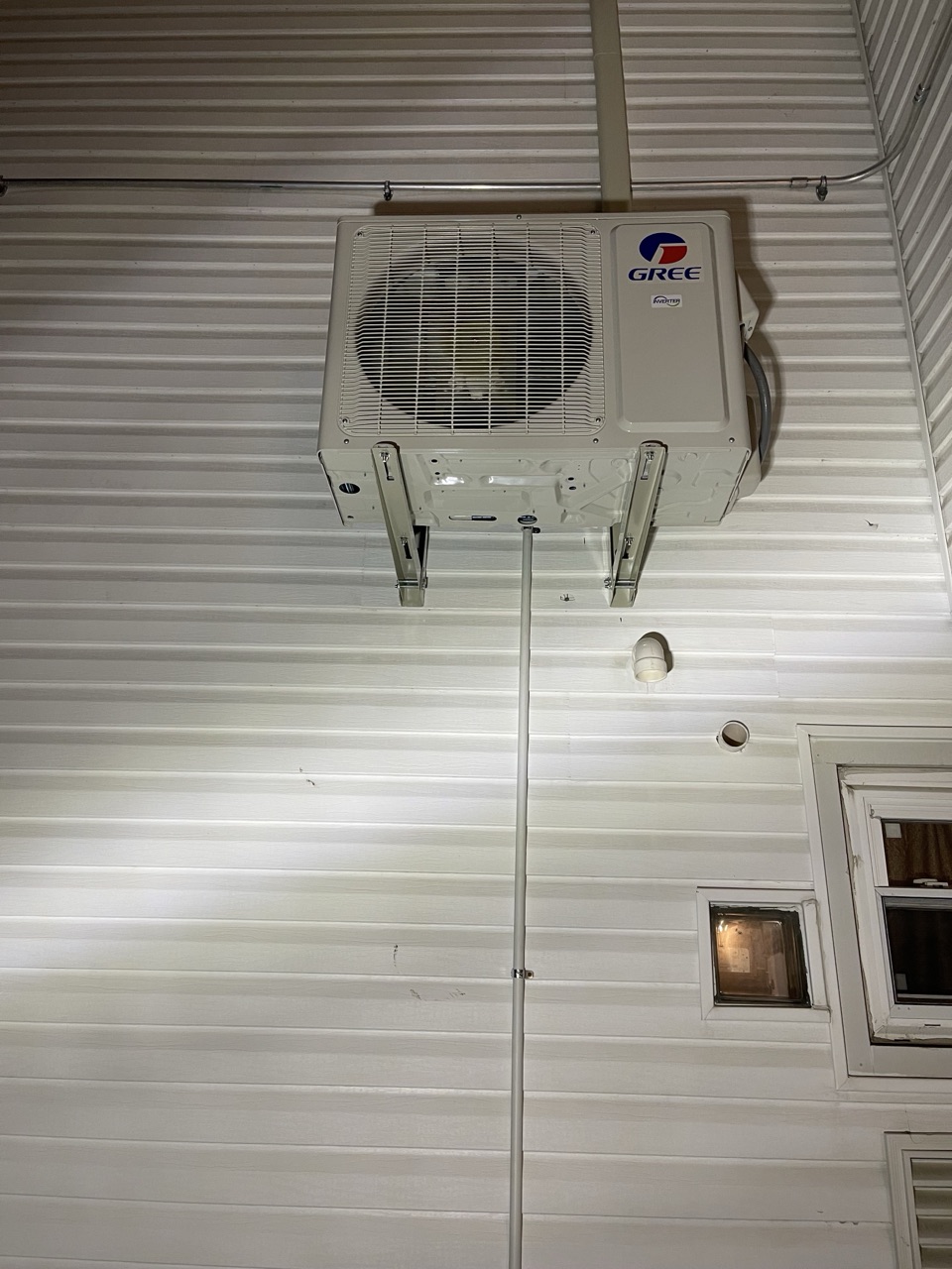 Gree outdoor condenser unit mounted on a white metal-sided building exterior at night