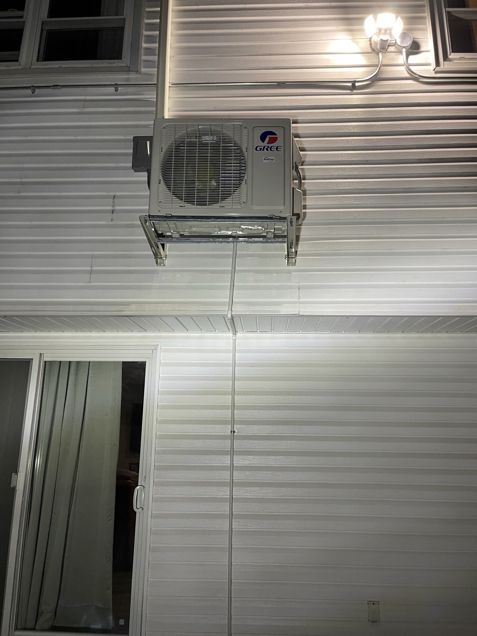 Gree outdoor condenser unit wall-mounted high above a sliding patio door on a Brooklyn home
