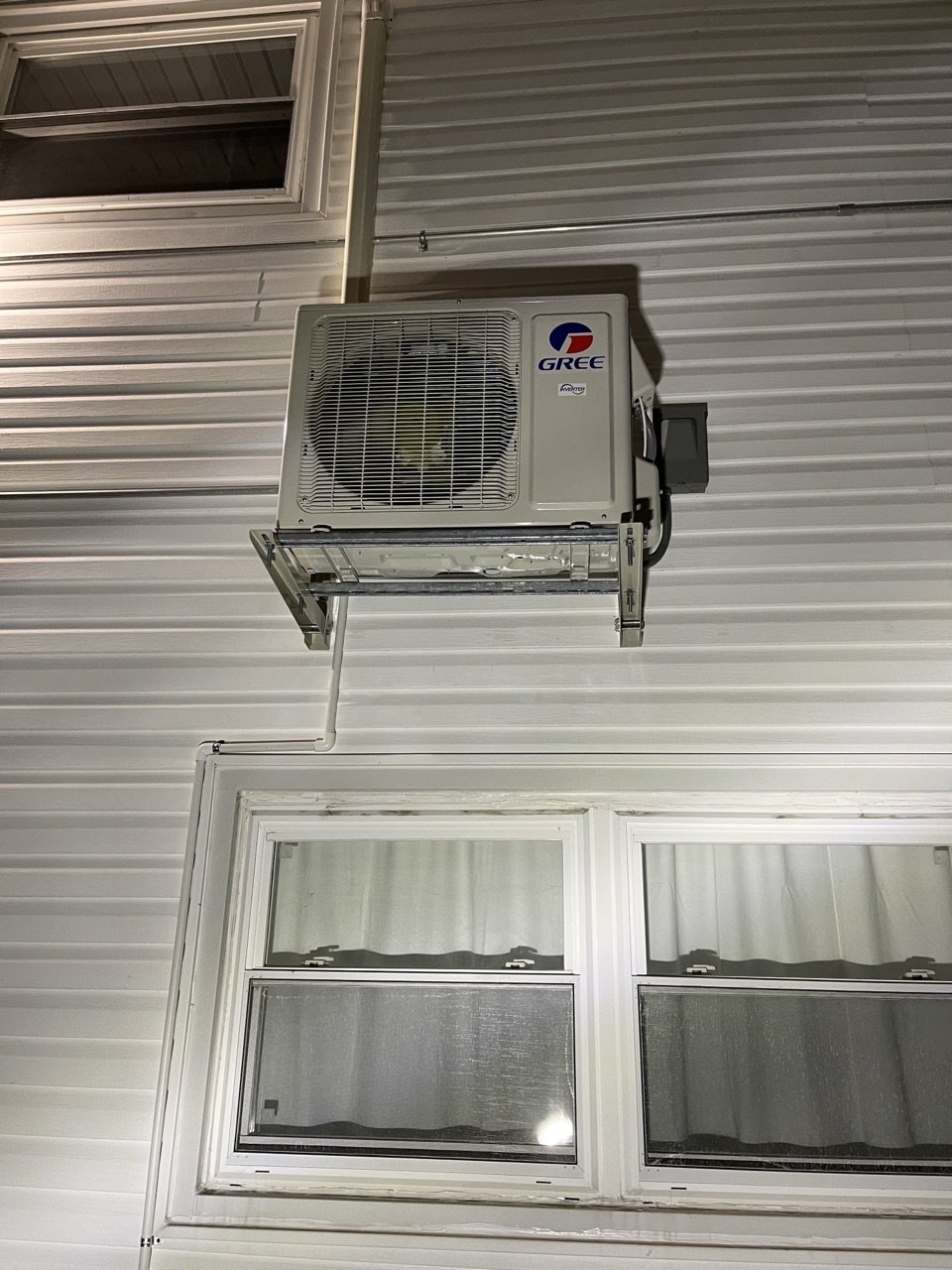 Gree outdoor condenser unit mounted high on a metal-sided wall above residential windows