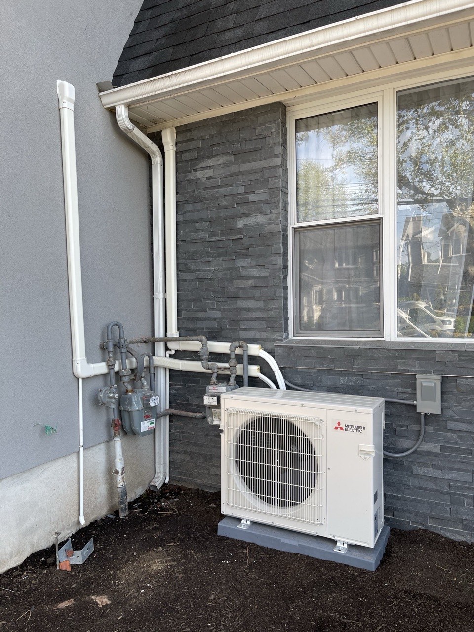 Mitsubishi Electric outdoor condenser unit installed against a stone-veneer wall next to a gas meter and downspout